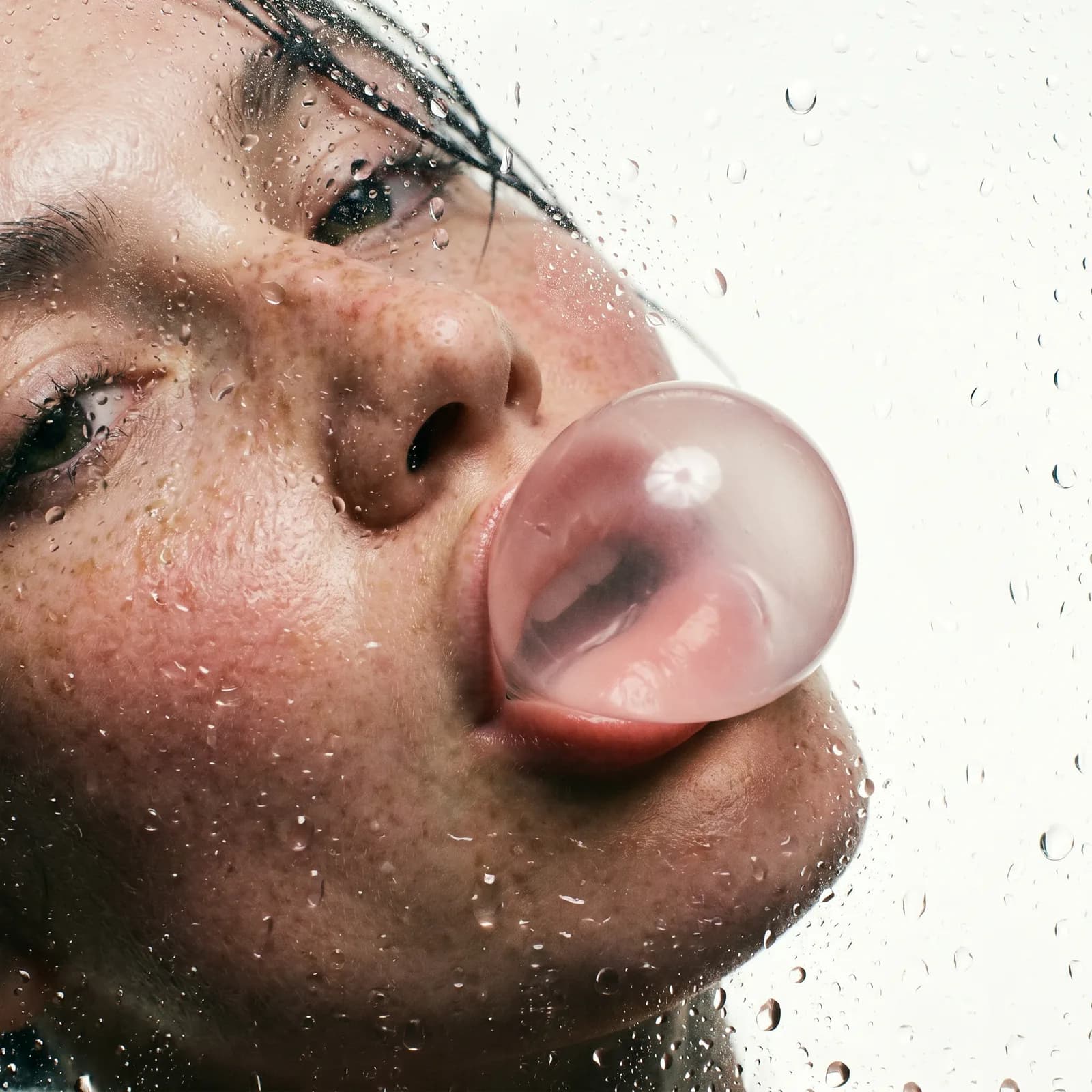 Close-up portrait behind wet glass of a model blowing a bubble-gum bubble