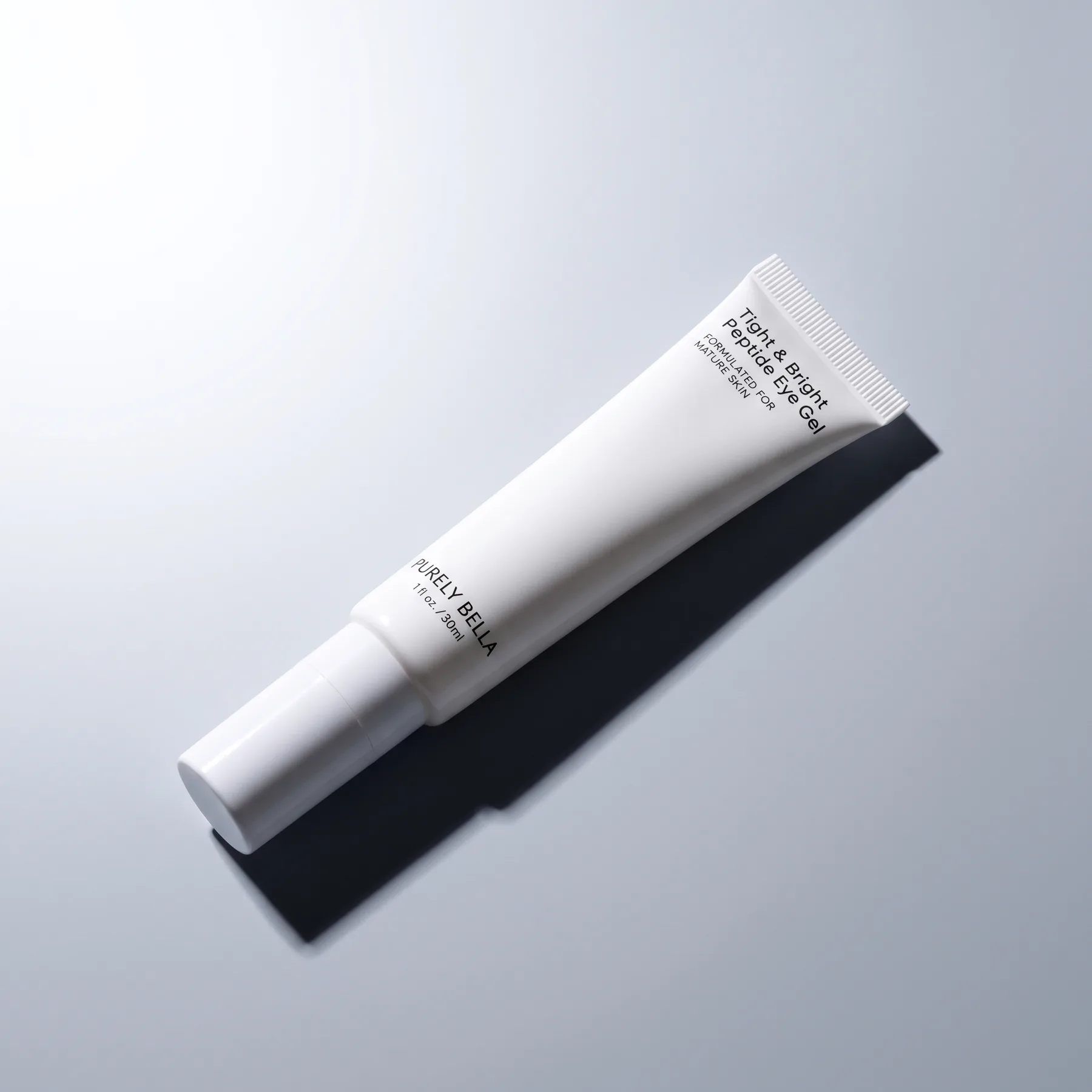 Single Purely Bella Tight & Bright Peptide Eye Gel tube on grey with a hard graphic shadow