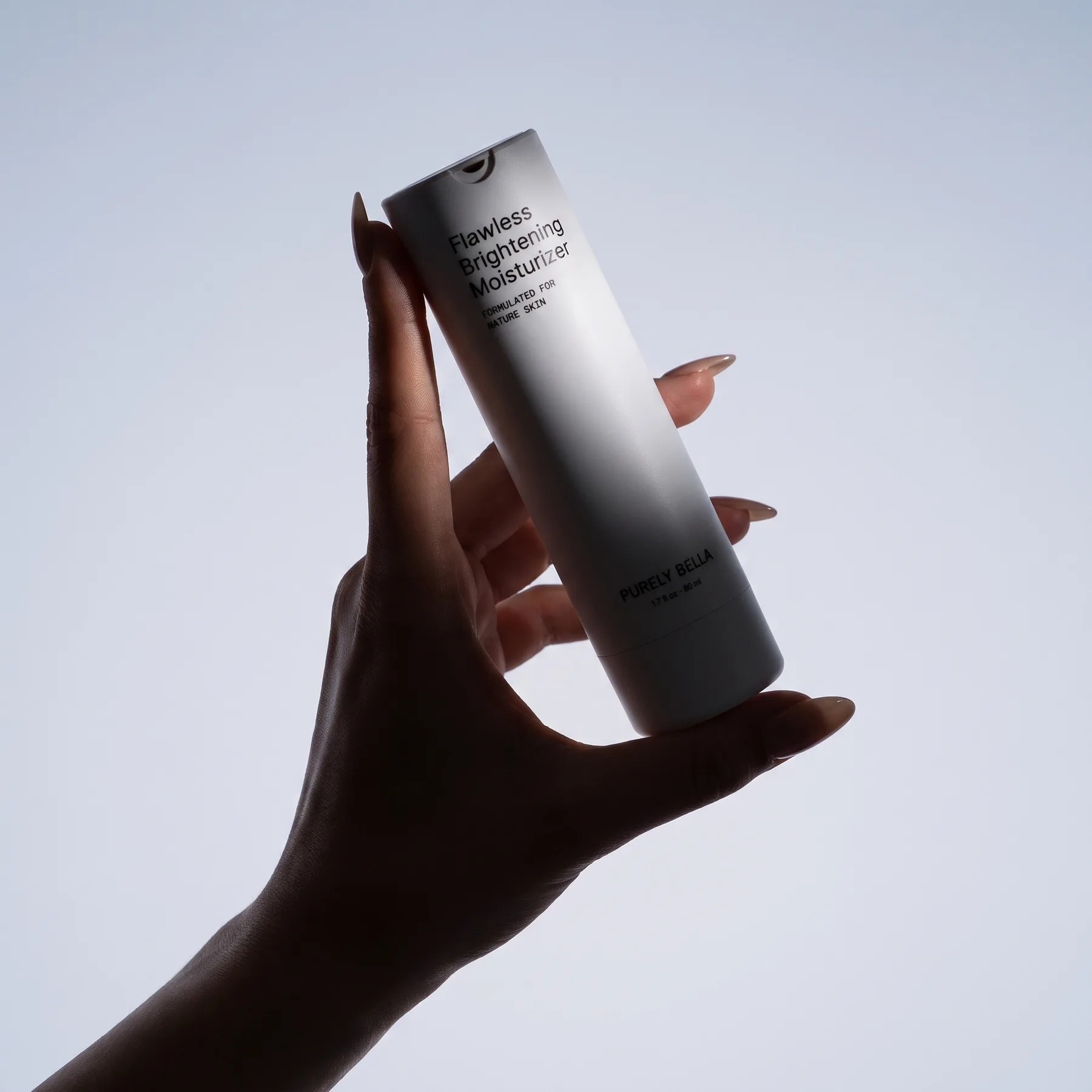 Hand holding the Purely Bella Flawless Brightening Moisturizer against a pale blue sky