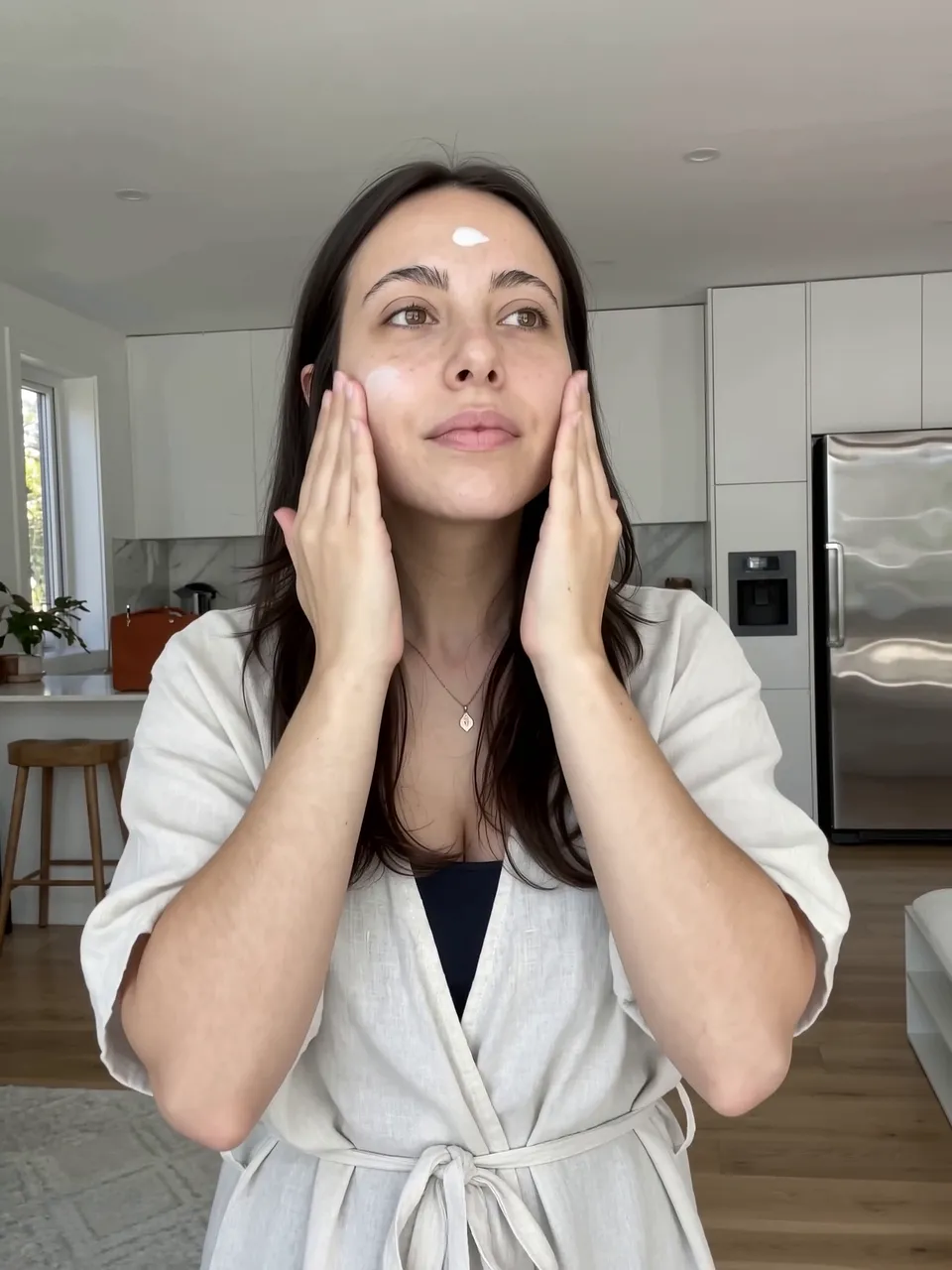 Creator in a white robe pressing lotion into her cheeks, frame from the AI UGC sample